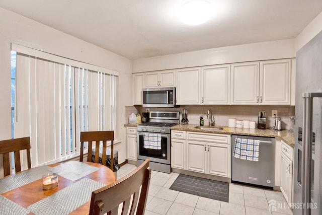 kitchen with light tile patterned floors, light stone countertops, stainless steel appliances, white cabinetry, and a sink