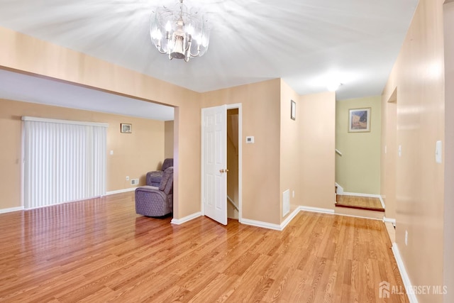 empty room with light wood finished floors, baseboards, stairway, and a chandelier