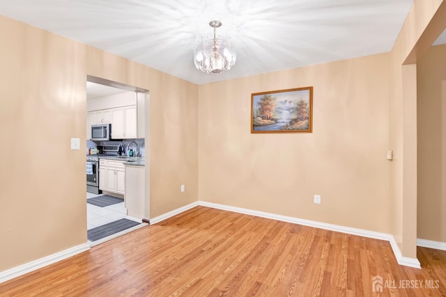 unfurnished dining area featuring baseboards, an inviting chandelier, and light wood-style floors