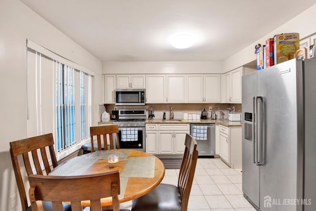 kitchen featuring light tile patterned flooring, stainless steel appliances, a sink, white cabinetry, and backsplash