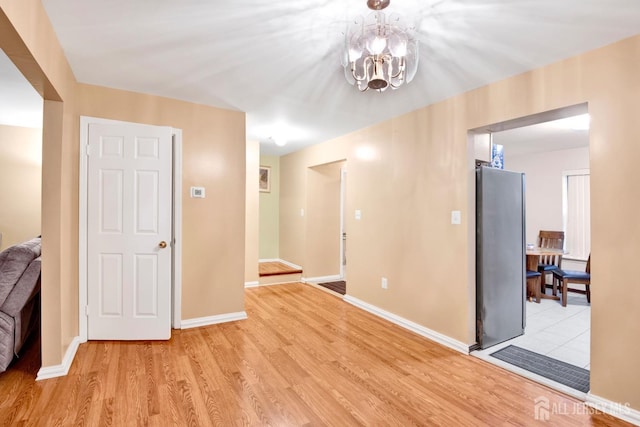 spare room featuring light wood-type flooring, a notable chandelier, and baseboards