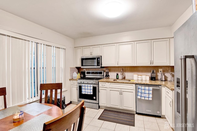 kitchen with white cabinets, appliances with stainless steel finishes, a sink, light stone countertops, and backsplash