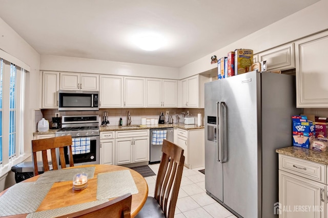 kitchen with stainless steel appliances, a sink, light stone countertops, and decorative backsplash