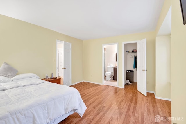 bedroom featuring baseboards, connected bathroom, light wood-style flooring, a walk in closet, and a closet