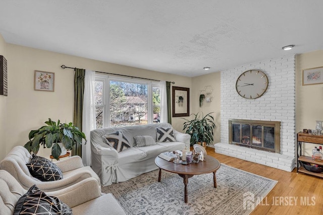 living area with a textured ceiling, a brick fireplace, and wood finished floors