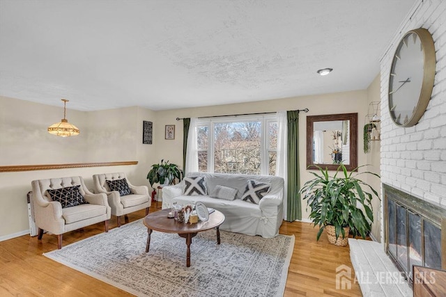 living room with baseboards, a brick fireplace, a textured ceiling, and light wood-style floors