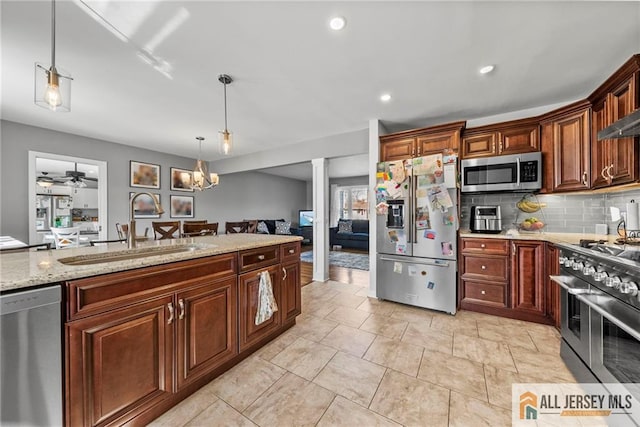 kitchen featuring hanging light fixtures, a sink, appliances with stainless steel finishes, decorative backsplash, and light stone counters
