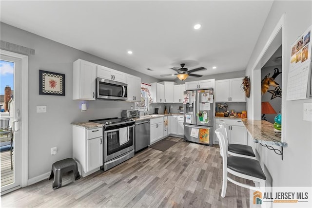 kitchen with light stone counters, light wood finished floors, a sink, white cabinetry, and appliances with stainless steel finishes