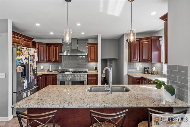 kitchen featuring wall chimney range hood, stainless steel appliances, a sink, and light stone countertops