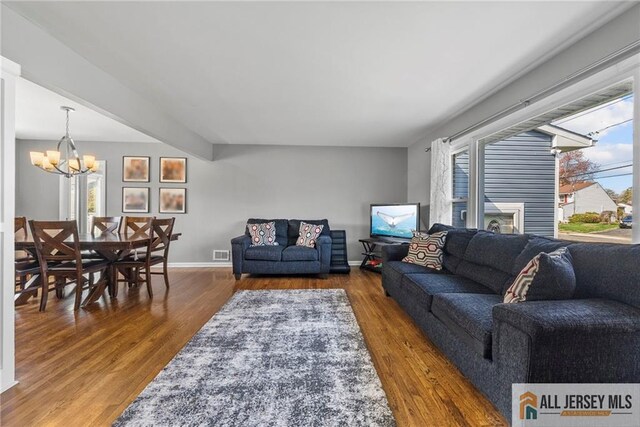 living area with baseboards, a notable chandelier, visible vents, and wood finished floors