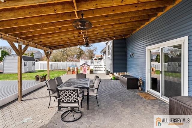 view of patio featuring fence, a deck, a storage unit, an outbuilding, and outdoor dining area