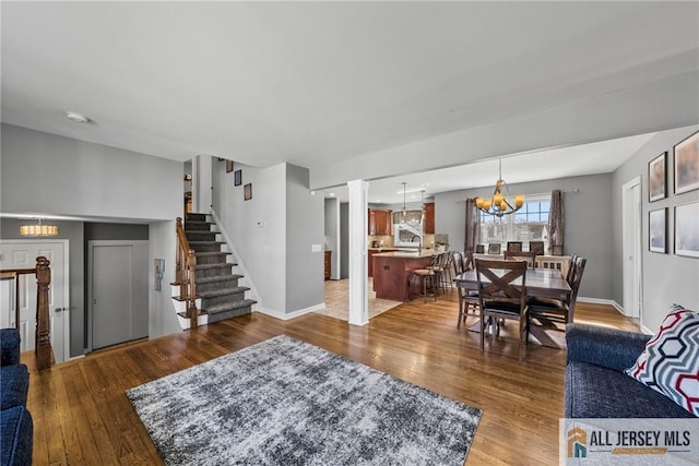 living room with wood finished floors, ornate columns, stairway, a chandelier, and baseboards