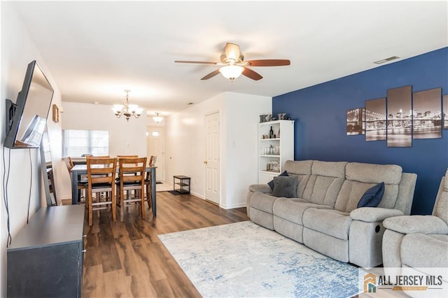living area featuring baseboards, visible vents, dark wood-style floors, and ceiling fan with notable chandelier