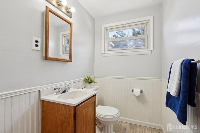 half bathroom with a wainscoted wall, toilet, vanity, and wood finished floors