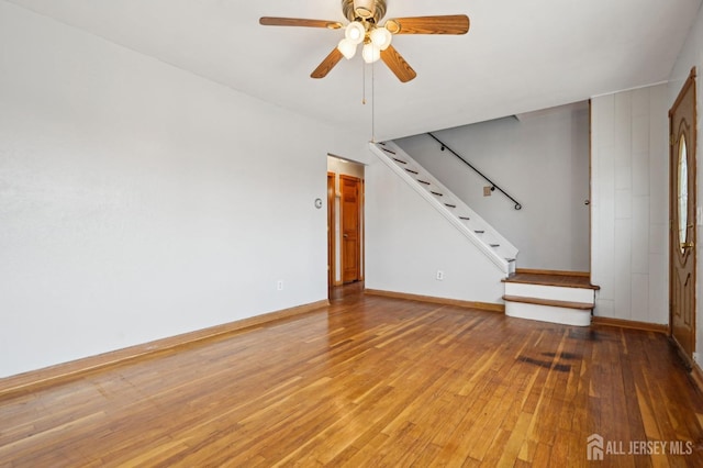 unfurnished living room with stairway, a ceiling fan, baseboards, and wood-type flooring