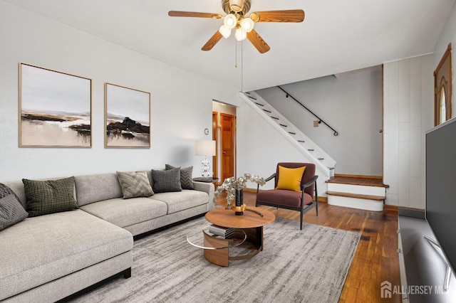 living area with wood-type flooring, a ceiling fan, and stairs