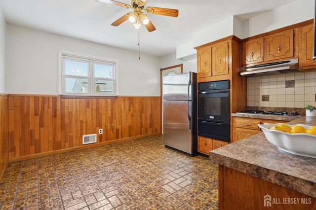 kitchen with wooden walls, under cabinet range hood, a wainscoted wall, stainless steel appliances, and a warming drawer