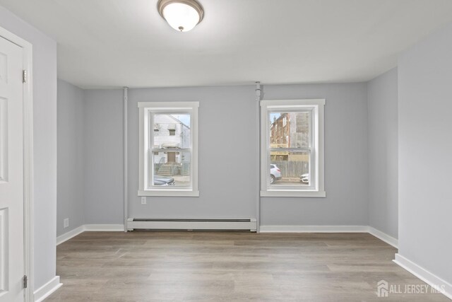 empty room with a baseboard heating unit, a healthy amount of sunlight, and light hardwood / wood-style floors