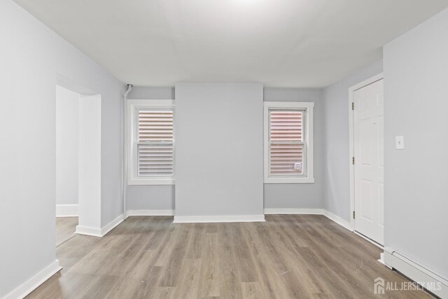 unfurnished room featuring baseboard heating, a healthy amount of sunlight, and light hardwood / wood-style floors