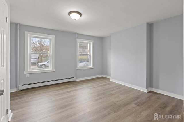 unfurnished room with a baseboard heating unit and light hardwood / wood-style flooring