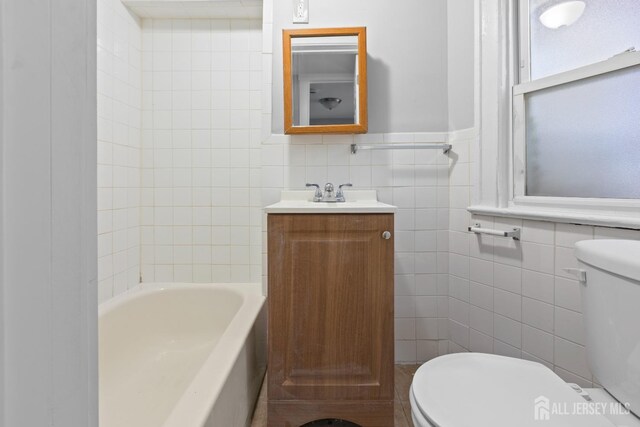 bathroom featuring toilet, vanity, tile walls, and a tub to relax in