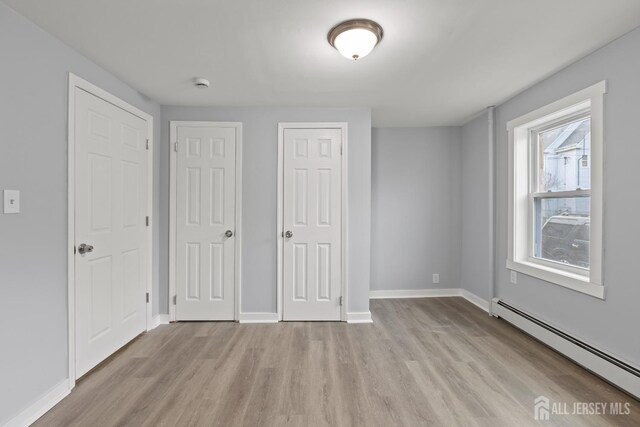 unfurnished bedroom with a baseboard heating unit and light hardwood / wood-style flooring