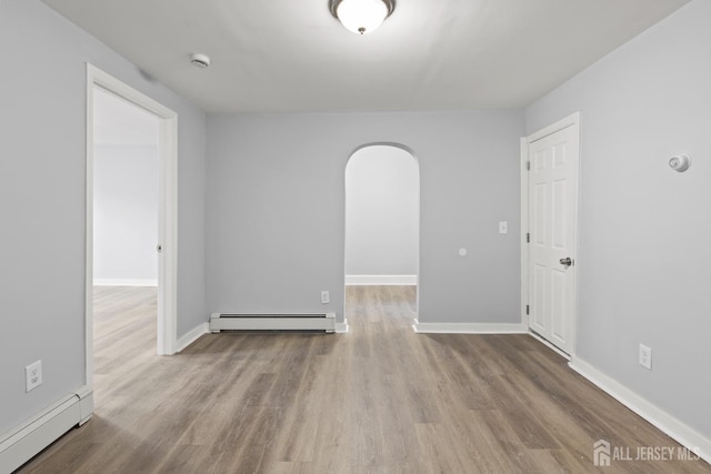 spare room featuring baseboard heating and light hardwood / wood-style flooring