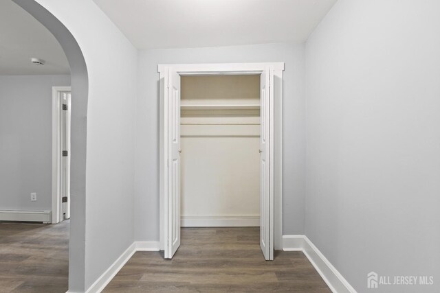 corridor with a baseboard heating unit and dark hardwood / wood-style flooring