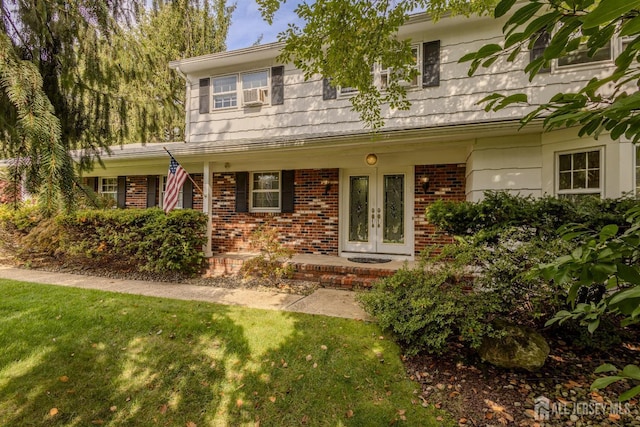 view of front of home featuring french doors, brick siding, a front lawn, and cooling unit