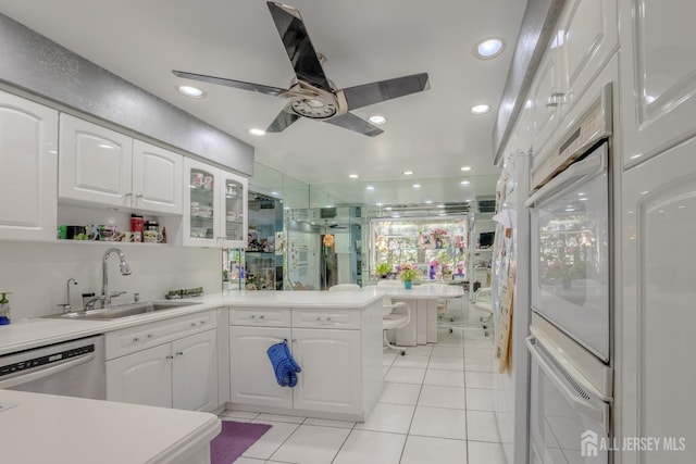 kitchen with a sink, a peninsula, light tile patterned floors, stainless steel dishwasher, and white cabinets