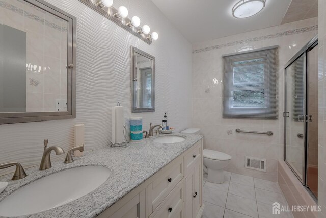 full bathroom with tile patterned floors, combined bath / shower with glass door, toilet, vanity, and tile walls