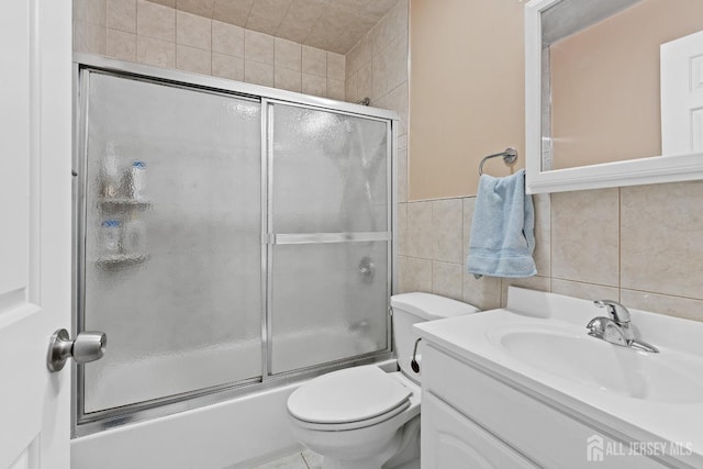 full bathroom featuring tile walls, vanity, bath / shower combo with glass door, and toilet