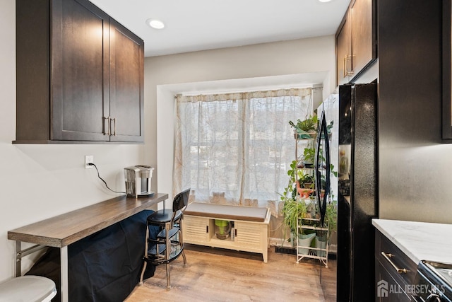 kitchen with light wood-type flooring, electric range oven, dark brown cabinets, and black fridge