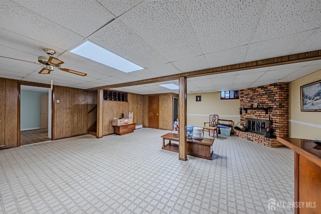 interior space with ceiling fan, a drop ceiling, a brick fireplace, and wood walls