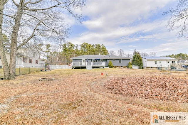 back of property with a yard, an outdoor fire pit, a wooden deck, and a fenced backyard