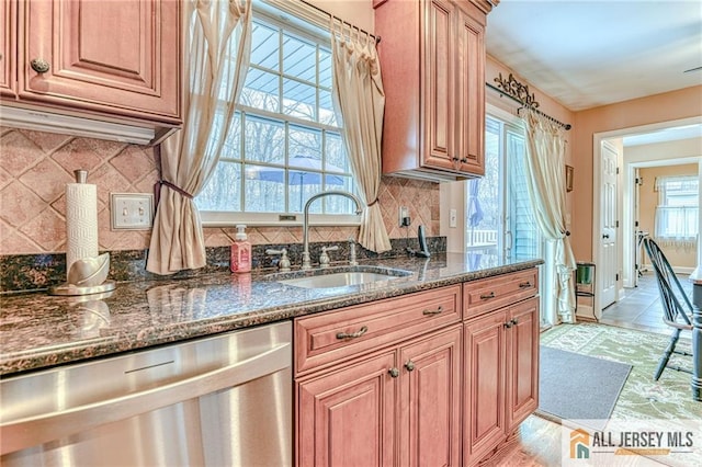 kitchen featuring a sink, dark stone countertops, backsplash, stainless steel dishwasher, and baseboards