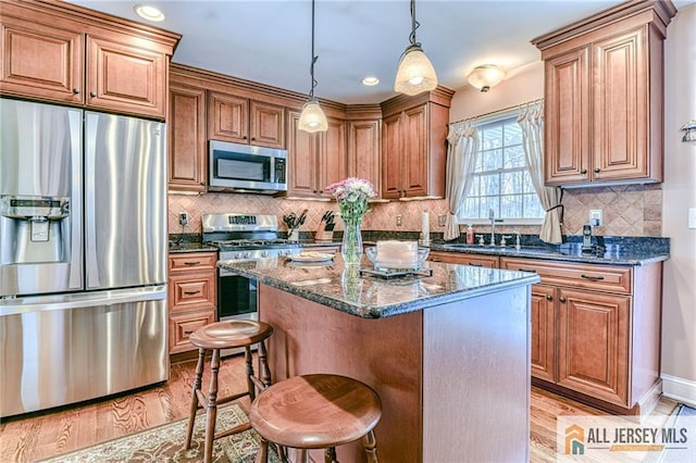 kitchen featuring a sink, a center island, dark stone counters, appliances with stainless steel finishes, and light wood finished floors