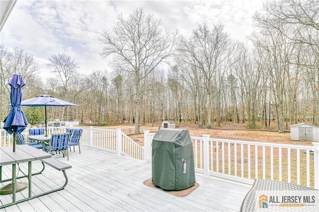 wooden terrace with an outdoor structure, a storage unit, outdoor dining area, and a grill