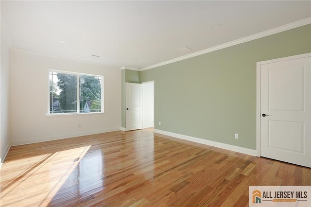 empty room with ornamental molding, light wood-type flooring, and baseboards