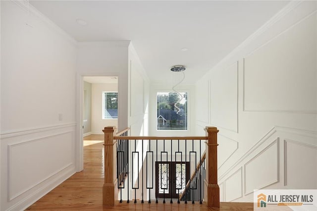 hallway featuring crown molding, a decorative wall, and an upstairs landing