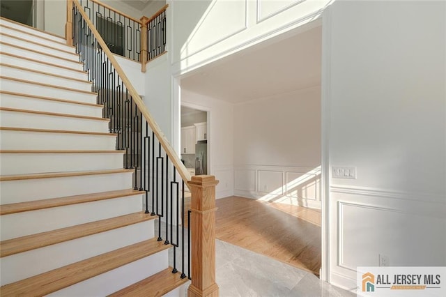 stairs featuring a wainscoted wall, a high ceiling, wood finished floors, and a decorative wall