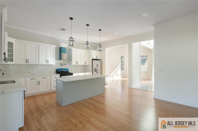 kitchen with stove, ornamental molding, stainless steel refrigerator with ice dispenser, backsplash, and wall chimney exhaust hood