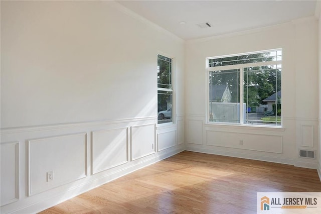 empty room featuring ornamental molding, light wood-type flooring, visible vents, and a decorative wall