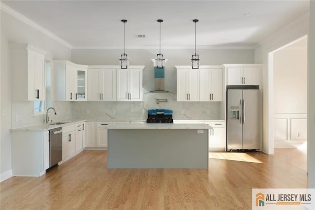 kitchen with light wood-style flooring, ornamental molding, stainless steel appliances, wall chimney range hood, and a sink