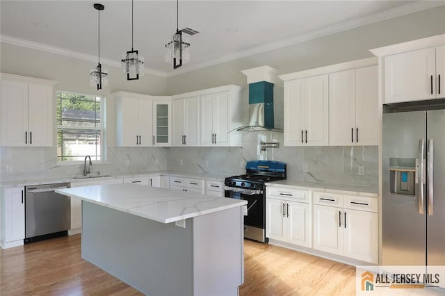 kitchen with stainless steel appliances, a sink, white cabinetry, light wood-style floors, and wall chimney exhaust hood