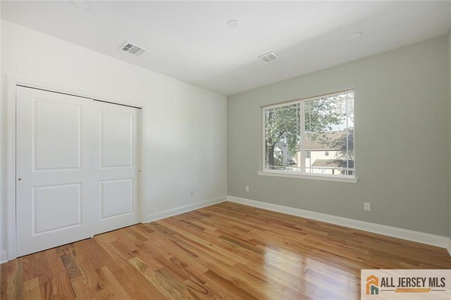 unfurnished bedroom featuring light wood-style flooring, a closet, visible vents, and baseboards