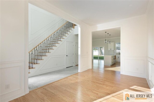 interior space with an inviting chandelier, ornamental molding, and light wood-type flooring