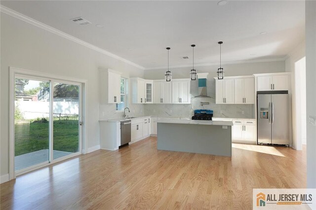 kitchen featuring appliances with stainless steel finishes, pendant lighting, white cabinetry, a center island, and wall chimney range hood