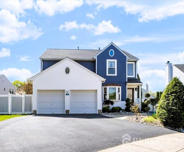 traditional home with a garage, fence, and aphalt driveway