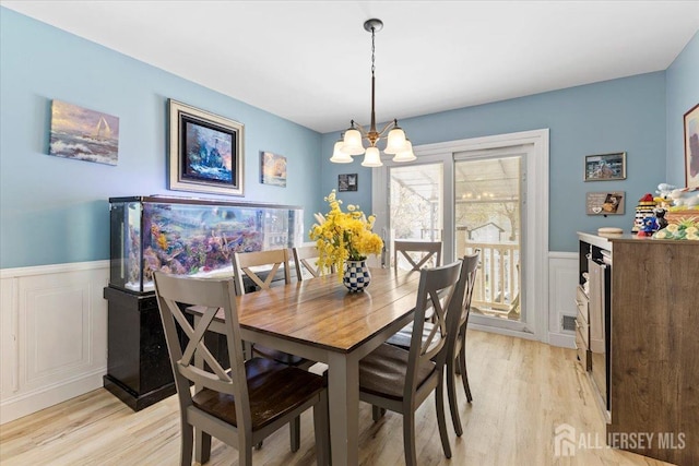 dining area featuring light wood-style floors, wainscoting, a decorative wall, and a notable chandelier